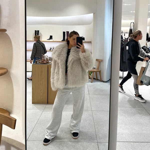 Person taking a mirror selfie wearing a fluffy white jacket and light gray pants in a store.