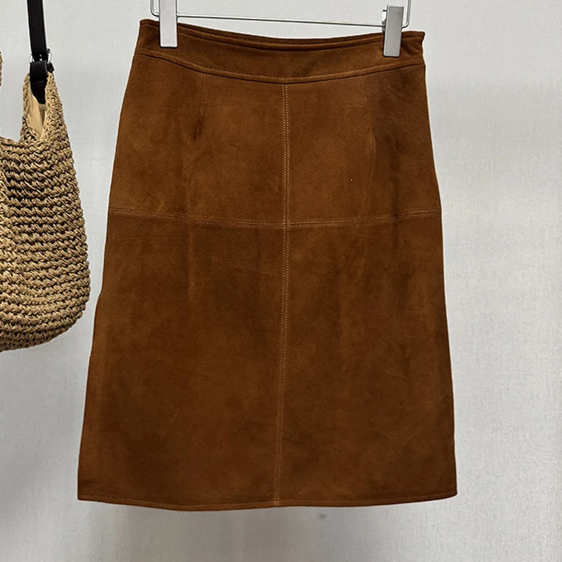 Brown suede skirt on a hanger with a straw bag in the background