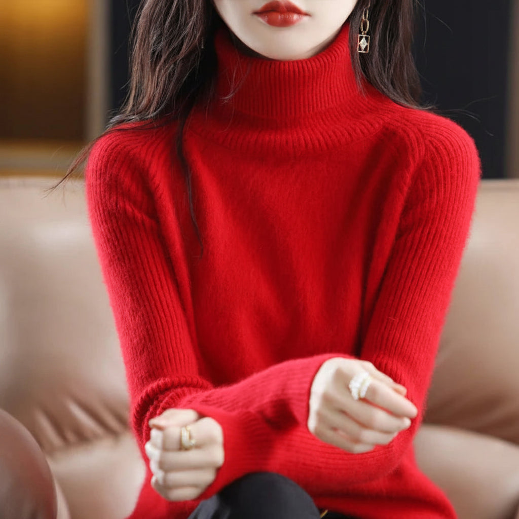 A woman wearing a bright red ribbed turtleneck sweater, seated on a beige leather sofa. 