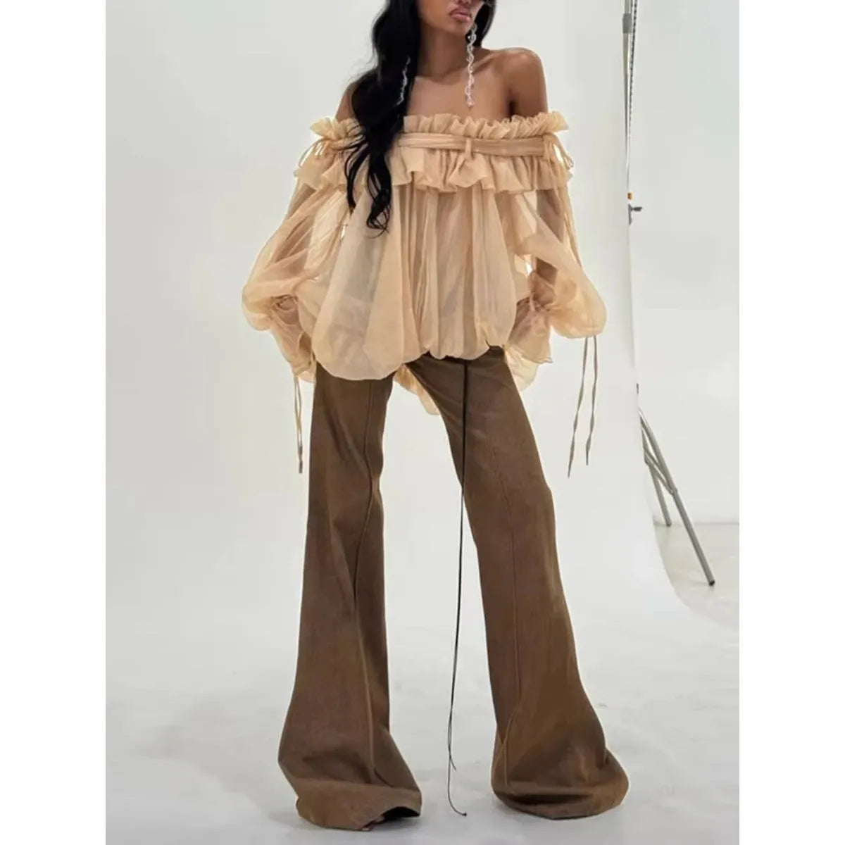 Woman wearing a beige off-shoulder top and brown flared pants against a white background