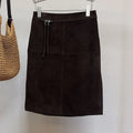 Deep Brown skirt on a hanger next to a woven bag against a white background