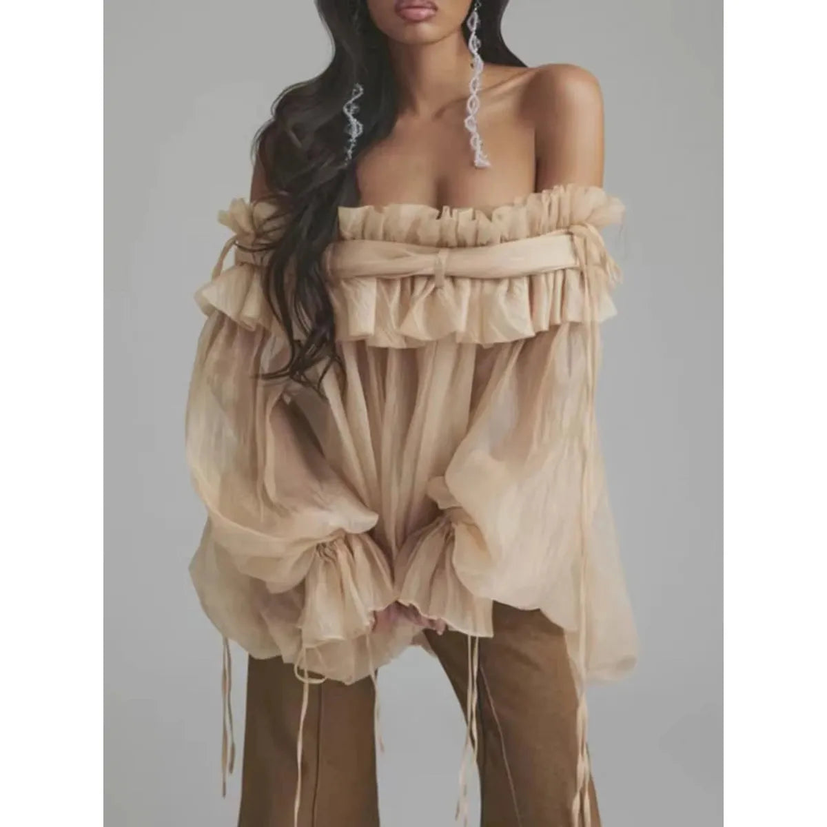 Woman wearing a beige off-shoulder top with ruffled layers against a gray background