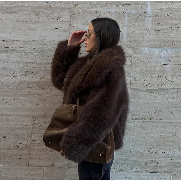 Woman wearing a brown fur coat against a stone wall.